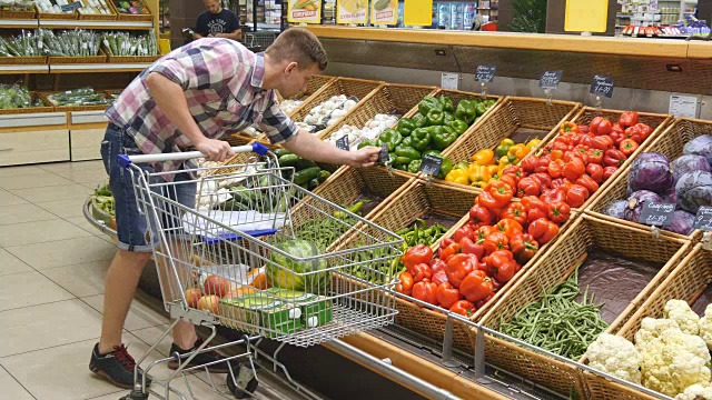 在超市里推着购物车的年轻人。有人在杂货店挑选新鲜蔬菜，然后把它们放进购物车。男孩在商店买辣椒视频下载