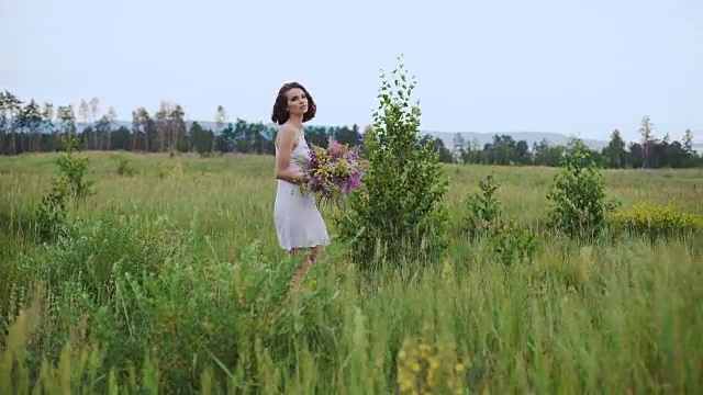 美丽而有灵感的女人在鲜花盛开的田野上与一束野花交谈视频素材