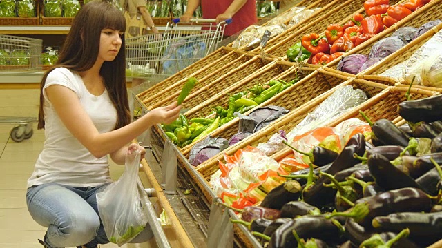 一个年轻漂亮的女孩在超市挑选辣椒。有魅力的女人在杂货店的农产品部门挑选新鲜的青椒。视频素材