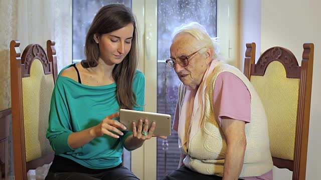 年轻女子教她的祖母用平板电脑工作-高级生活方式视频素材