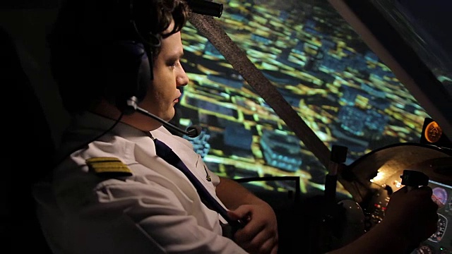 穿着漂亮制服的商业飞行员在夜晚的城市上空控制飞机视频素材