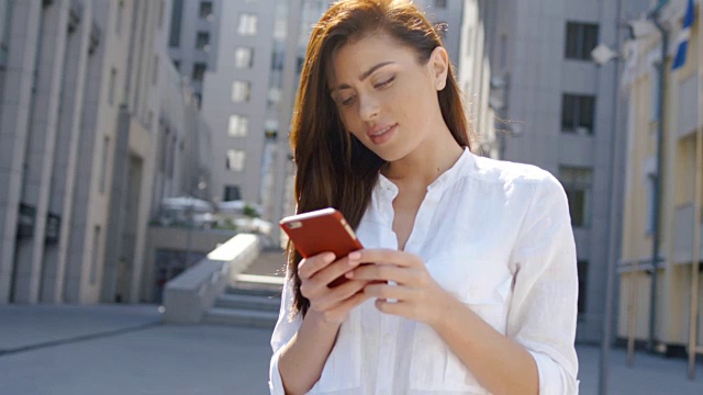 年轻迷人的黑发女子在城市街道上用智能手机发短信。都市人生活方式背景视频下载