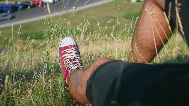 一个男人的腿躺在路边小山上的草地上视频下载