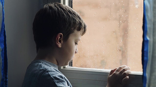 一个忧郁而悲伤的孩子在雨天用手指在湿漉漉的窗户上玩视频素材