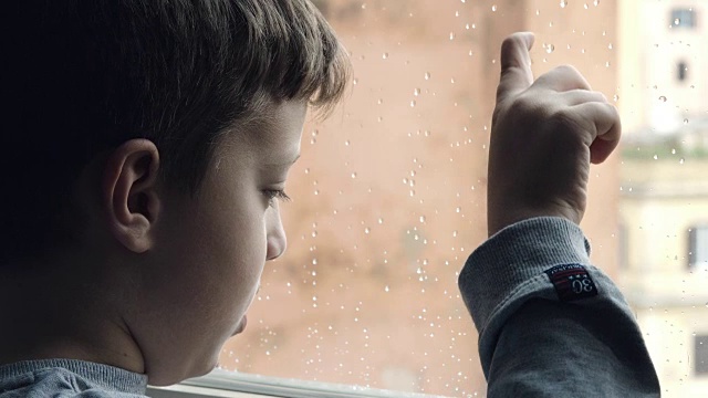 玩着雨滴打在窗户上:下雨天悲伤的小孩子视频素材