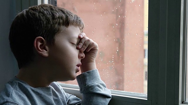 可怜的孩子在雨天望着窗外视频素材