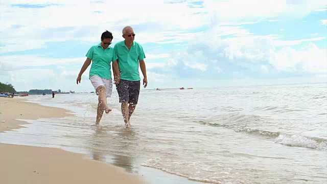 一对退休的亚洲老夫妇在美丽天空下的热带海滩上散步视频素材