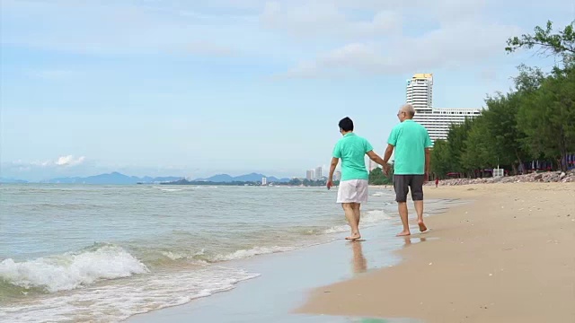 一对退休的亚洲老夫妇在美丽天空下的热带海滩上散步视频素材