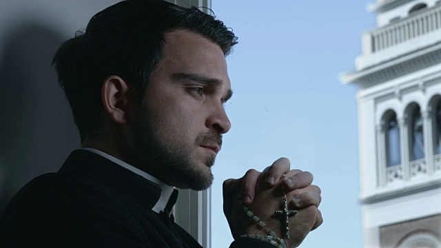 年轻的牧师用手中的念珠祈祷:钟楼的背景视频下载