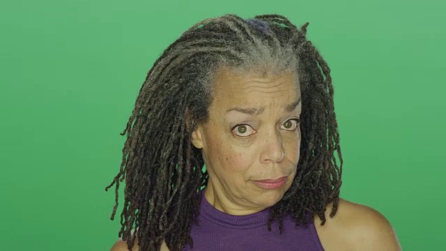 在一个绿色屏幕的演播室背景上，一个留着雷鬼辫的年长非洲裔美国妇女微笑着，然后看起来很惊讶视频素材