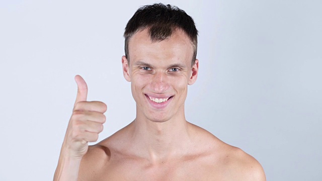 微笑的年轻裸胸男子的肖像与拇指向上视频下载