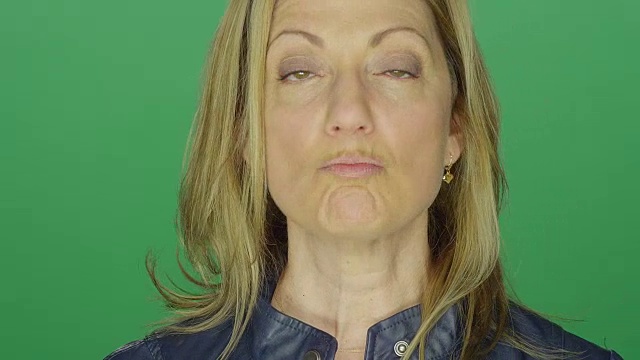 美丽的中年妇女做滑稽的脸，在一个绿色屏幕的工作室背景视频素材