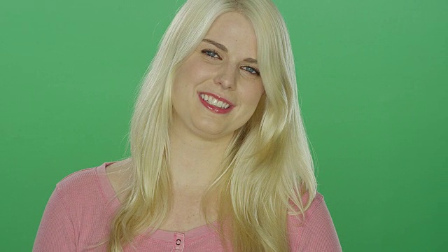美丽的金发女子与蓝色眼睛微笑，在一个绿色屏幕的工作室背景视频素材