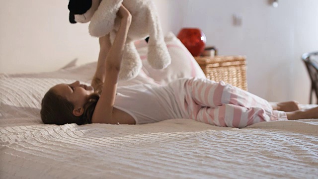 可爱活泼的女孩坐在床上，玩柔软的狗玩具视频素材