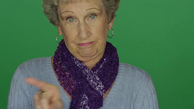 在一个绿色屏幕的演播室背景上，一个老女人来回地摇着她的手指视频素材