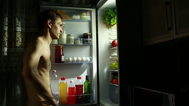 守夜人站在打开的冰箱旁。吃三明治。饥饿的人视频下载
