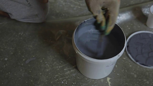 建筑工小心翼翼地把灰色的油漆搅拌在塑料桶里，涂在墙上视频素材