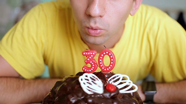 一个男人吹灭了一个有蝴蝶翅膀的巧克力蛋糕上30年的蜡烛。这个人今天过生日视频下载