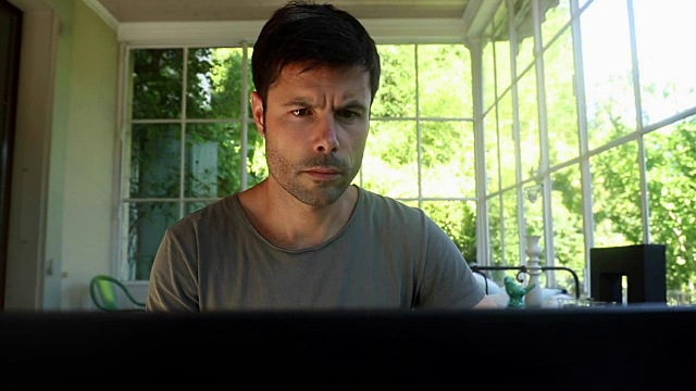 在家里工作的人看着电脑屏幕。一个30多岁的男人在阳台上看笔记本电脑的特写视频素材