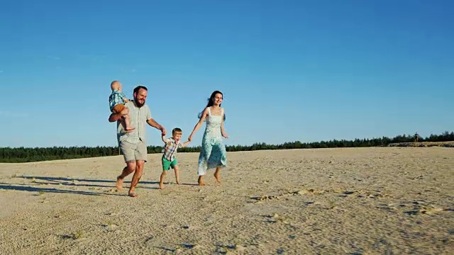 斯坦尼康镜头:欢乐的一家人在沙滩上奔跑。父母和两个年幼的儿子视频素材