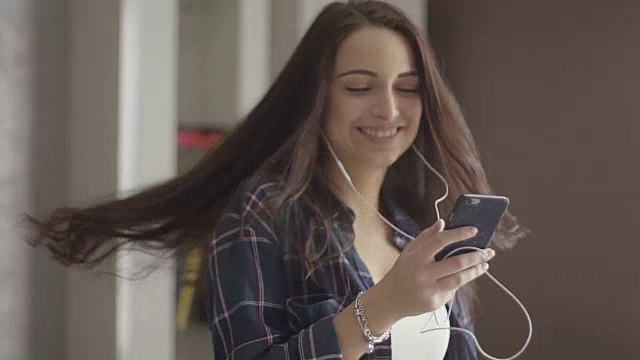 音乐和科技概念-微笑的少女穿着格子衬衫戴着耳机听mp3在家里跳舞视频下载