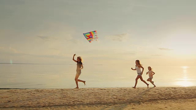 妈妈带着两个女儿在沙滩上放风筝。乐趣在一起。快乐的童年视频素材