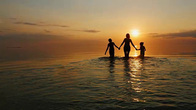 夕阳西下，母亲带着两个孩子去海里游泳，笑着视频素材