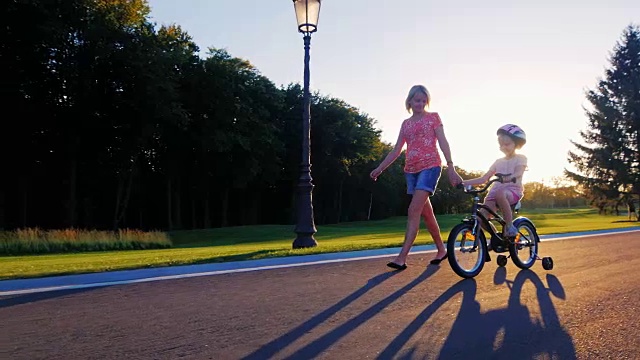 妈妈和女儿在公园散步。妈妈牵着她的手，一个孩子骑着自行车走近视频素材
