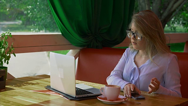 女商人戴着眼镜在咖啡馆工作，用智能手机聊天视频素材
