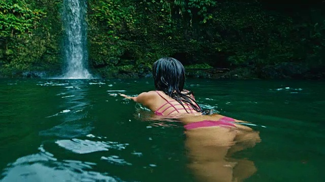 年轻女子游泳到瀑布视频素材