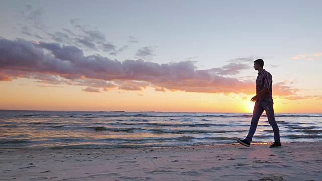 斯坦尼康慢镜头:年轻的孤独男子走在日落的海边视频下载