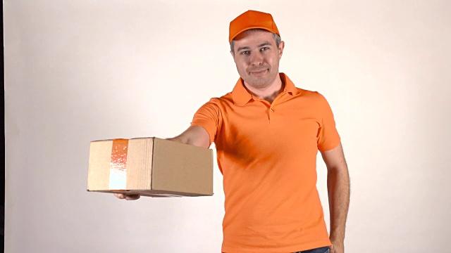 穿着橙色制服的帅气快递员一边打电话一边送包裹。浅灰色背景，全高清工作室灯光拍摄视频下载
