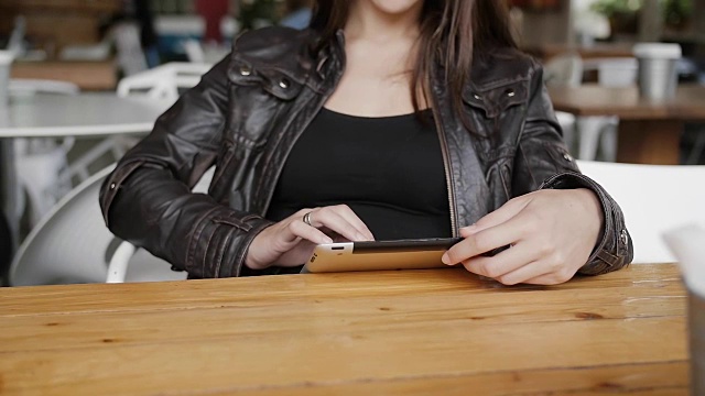 时尚的年轻女子坐在现代咖啡馆的桌边，用平板电脑发送短信，惊讶地看着，微笑着视频素材