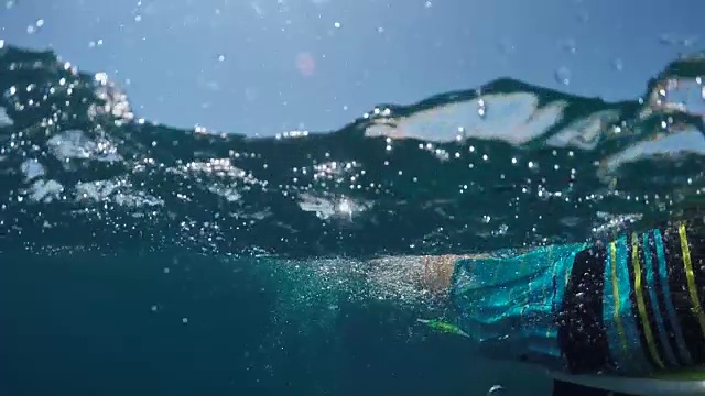 水下慢动作:一个年轻的冲浪者在开放水域的海浪上划桨视频素材