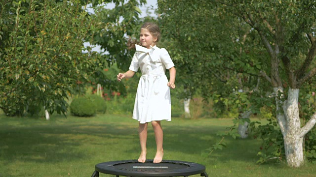 那个可爱的女孩在花园里的蹦床上蹦蹦跳跳视频素材
