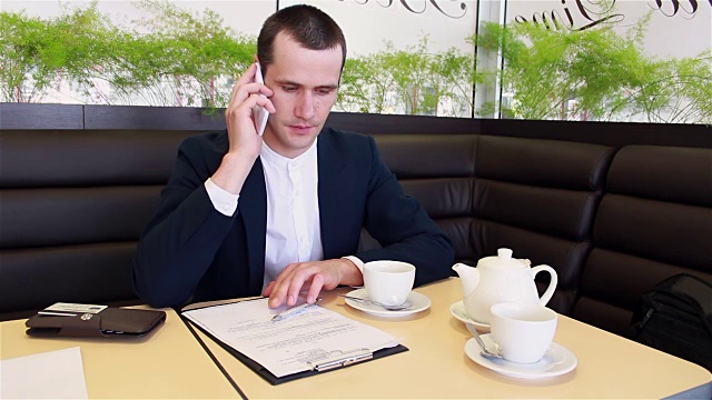 年轻的商人坐在咖啡馆里一边喝咖啡一边讲电话视频素材