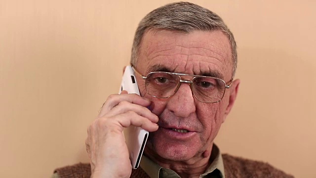 一位拿着白色智能手机的老人一边说话一边微笑视频下载