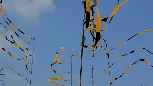 一套明亮的黄色黑丝带旗在风中飘扬，以蓝色的天空为背景视频下载