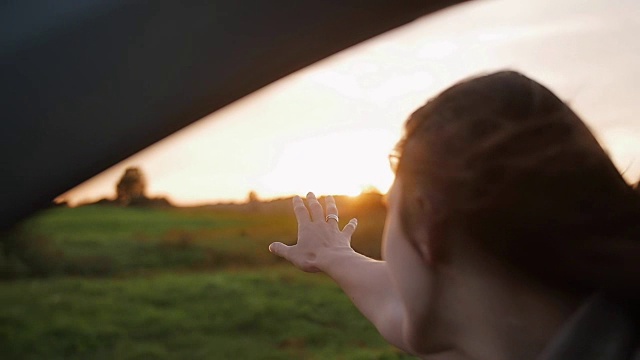 幸福-年轻女子在车里，手在空中玩。大自然中美丽的日落。风吹头发。缓慢的莫视频下载