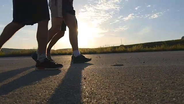 日落时分，男性的脚正走在乡间小路上。三个男人走在一条空旷的乡间小路上。一个穿过阳光照耀的路线的人。小男孩们的双腿在小路上移动。生活方式,特写视频素材