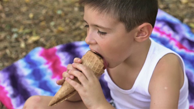 在公园里，小男孩用舌头舔冰淇淋视频素材