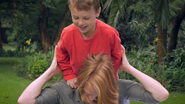 一个妈妈让她可爱的笑着的儿子坐在她的肩膀上玩——慢动作视频素材