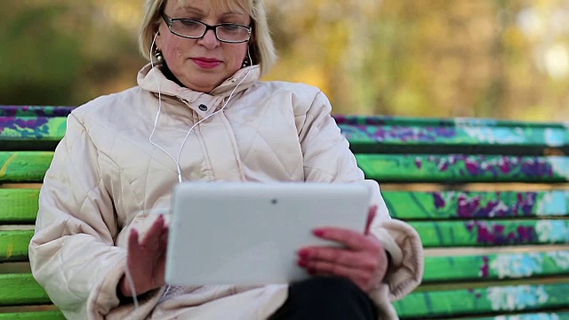 女人坐在长凳上使用平板电脑。拥有平板电脑的女性视频素材