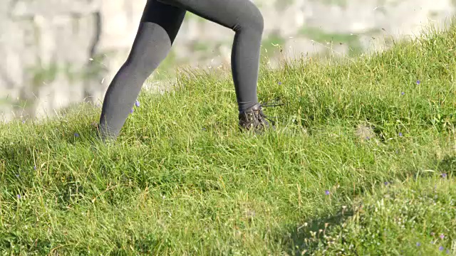 慢镜头:女登山运动员穿着山靴走在开花的草地上视频素材