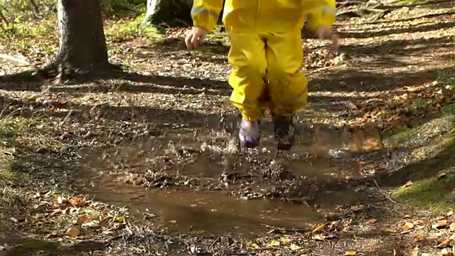 穿着黄色橡皮服的小女孩正在水坑里跳。慢动作视频下载