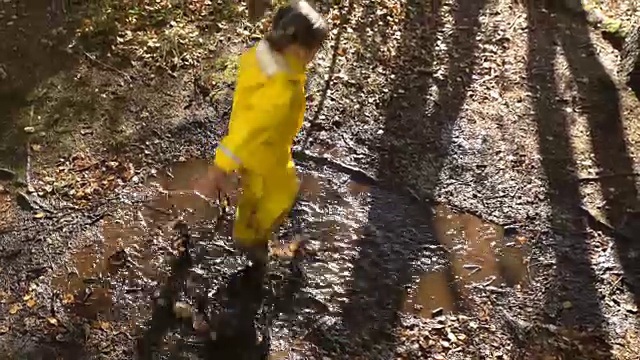 穿着黄色橡皮服的小女孩正在水坑里跳。视频下载