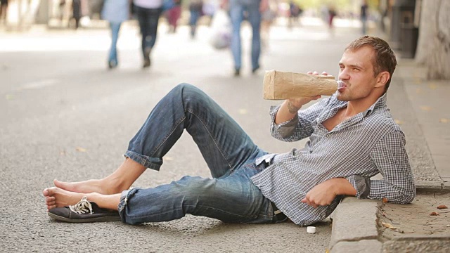一个醉汉躺在外面的人行道上。一个男人从纸袋里喝啤酒视频下载
