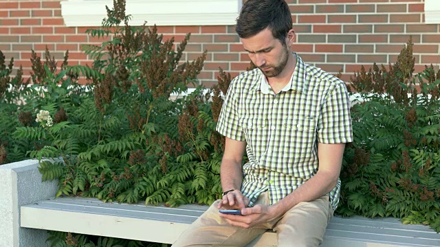 一个穿着休闲的男人坐在长椅上玩手机视频素材