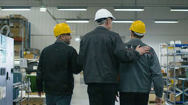 后视图高级工程师和两个工人正在走过工厂空间的文件。视频素材
