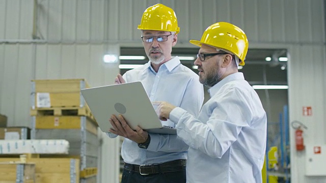 物流中心仓库的两名员工正在讨论工作，手里拿着一台笔记本电脑。视频素材